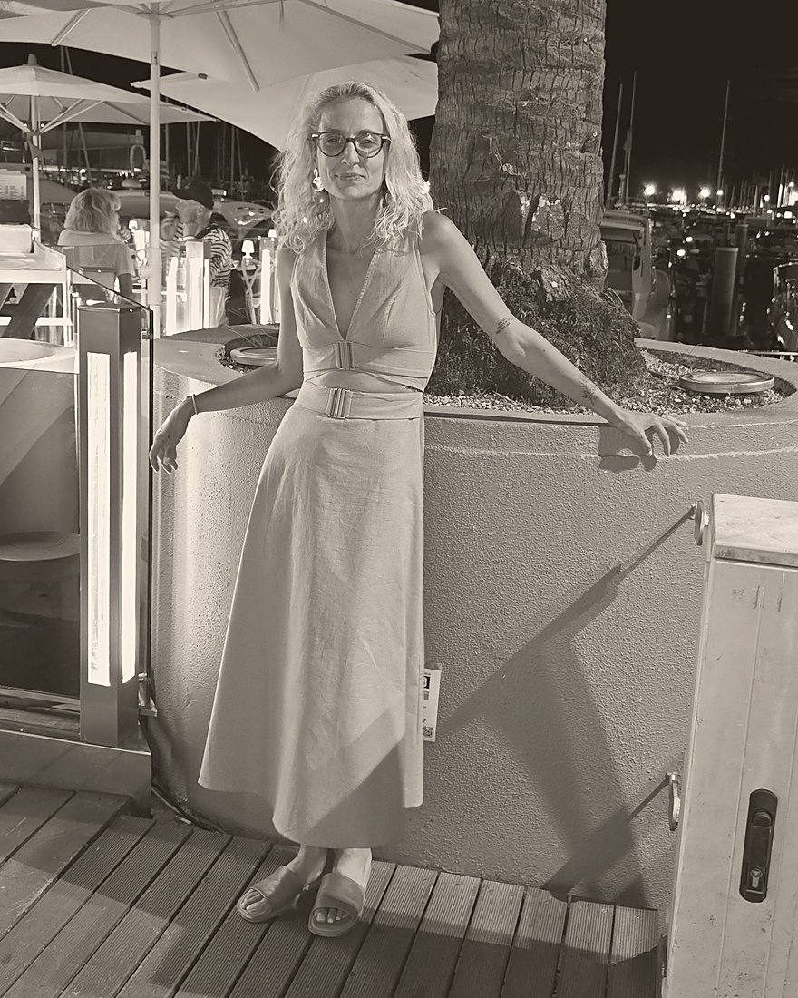 Black-and-white photo of Jessi at a marina at night, leaning on a palm planter
